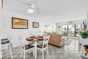 A dining area with a round table, white chairs, and a ceiling fan.