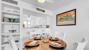 A dining area with a round table, white chairs, and a framed picture on the wall. - Runaway Bay 283 by Duncan Real Estate (Bradenton Beach)