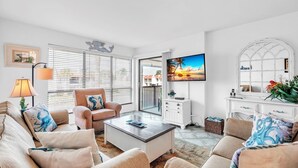 A living room with a sofa, armchair, coffee table, TV, and a balcony with a view. - Runaway Bay 283 by Duncan Real Estate (Bradenton Beach)