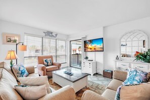 Sala de estar com sofá, poltrona, mesa de centro, televisão e varanda com vista.