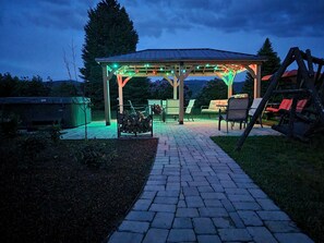 Ein überdachter Außenbereich mit einer Pergola, einem Feuerkorb und einem Holzstoß.