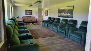 Un salón amplio con una hilera de sillones verdes, un sofá marrón y piso de madera.