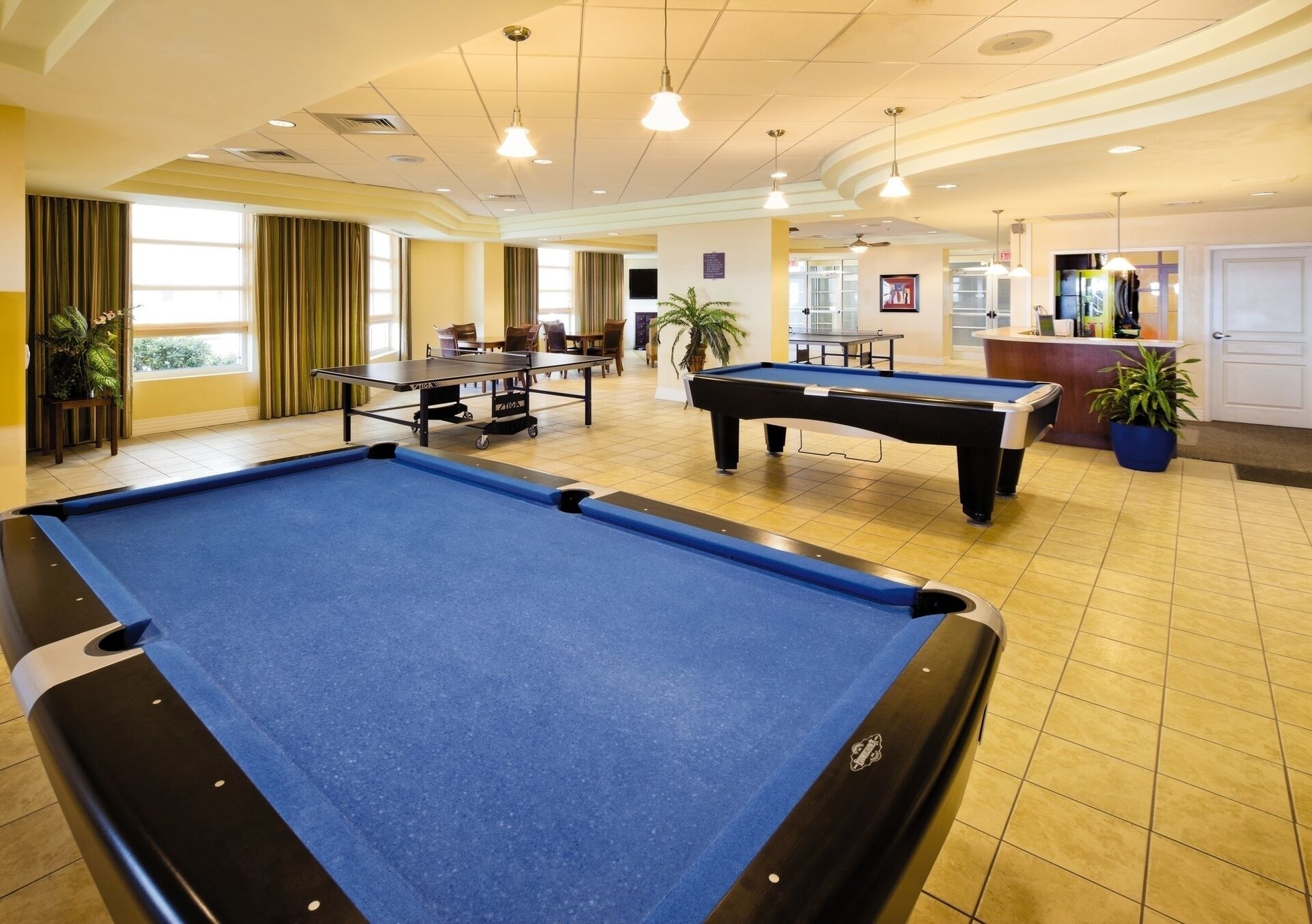 Une table de billard dans un espace intérieur bien éclairé, avec un comptoir d’accueil et un coin salon.