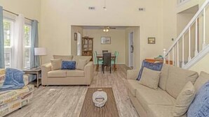 Una amplia sala de estar con techo alto, un comedor con mesa y sillas, y una escalera que conduce a un piso superior.