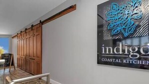 A hallway with a wooden door, a metal railing, and a sign for 'indigo Coastal Kitchen'.