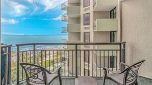 A balcony with a view of the ocean, two chairs, and a table.