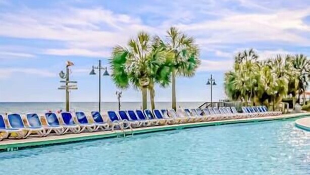 A pool with blue lounge chairs and palm trees.