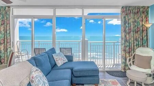 A room with a large sliding glass door leading to a balcony with a view of the ocean. - Stay on the Boardwalk | Oceanfront w/ Pools! (Myrtle Beach)