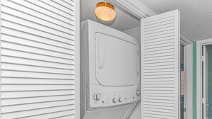 Ett tvättrum med en tvättmaskin och en torktumlare som man fyller på framifrån, en lampa ovanför tvättmaskinen och en dörr som leder till ett annat rum.