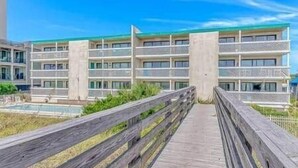 Ett hotell med flera våningar och balkonger, en träpromenad som leder till entrén och en klarblå himmel.