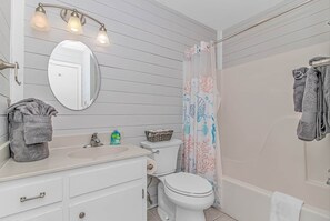 A bathroom with a white sink, mirror, toilet, and shower curtain.
