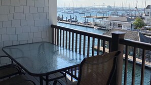 Ein Balkon mit Glastisch und St ühlen, der auf einen Yachthafen mit Booten und einer Brücke blickt.