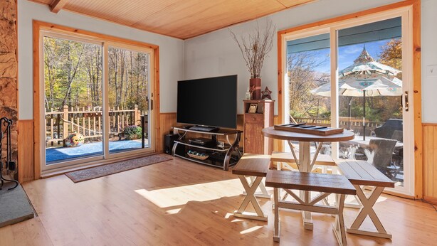 A spacious living room with a wooden floor, a flat-screen TV, a wooden table with benches, and large sliding glass doors leading to an outdoor deck. - Big Indian near
 Full Moon Resort Spillian Onteora Mountain House Ski Belleayre  (Big Indian)