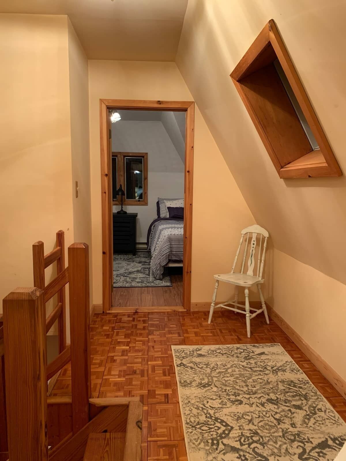 Un couloir étroit, doté d’un plancher en bois et d’un tapis à motifs. Une chaise blanche est placée contre le mur.