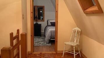 Un couloir étroit, doté d’un plancher en bois et d’un tapis à motifs. Une chaise blanche est placée contre le mur.