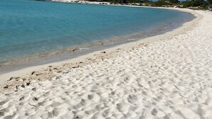 Una playa con aguas azul turquesa, arena blanca y una costa distante con vegetación.