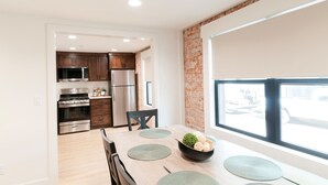 A modern kitchen with stainless steel appliances, a dining area with a large window, and a brick accent wall.