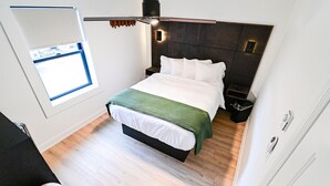 A modern bedroom with a bed, a bedside table, a nightstand, a small window, and a ceiling light fixture.