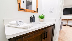 A bathroom with a white sink, dark wooden cabinets, a mirror with a wooden frame, a small potted plant, and a towel on the counter.