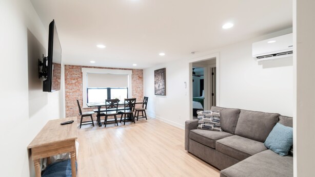 A modern living room with a dining area, a grey sofa, and a flat-screen TV mounted on the wall.