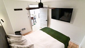 A bedroom with a bed, a green throw, a mounted TV, and a door leading to a bathroom.