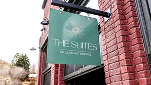 A green sign with white text reading "THE SUITES OF LAVA HOT SPRINGS" hanging from a building.