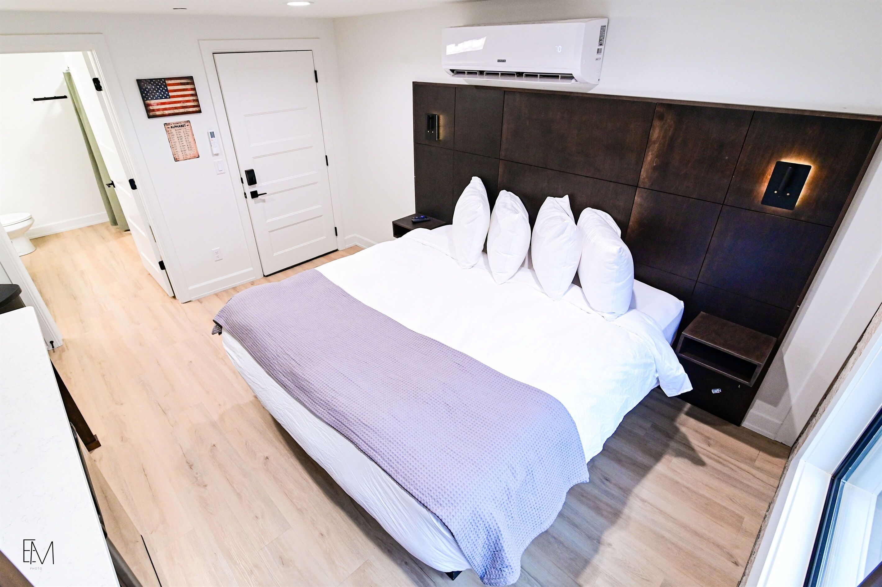 A hotel room with a large bed, a headboard with built-in lighting, a bedside table, and a wall-mounted air conditioner.