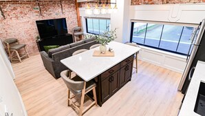 Een moderne keuken met een groot eiland, donkere kastjes en een accentmuur van baksteen.