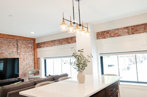 A modern kitchen with a brick wall, a large island, and a hanging light fixture. - Idaho Falls Theme- Suites of Lava #7 (Lava Hot Springs)