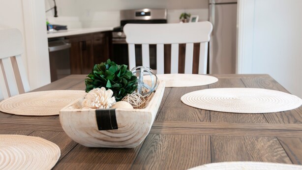 A wooden dining table with a centerpiece of a white bowl containing a plant and decorative items.