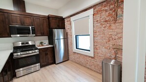 A kitchen with wooden cabinets, stainless steel appliances, a brick wall, and a window.