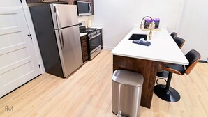 Une cuisine moderne dotée d’appareils électroménagers en acier inoxydable, d’un plan de travail blanc et de meubles en bois.