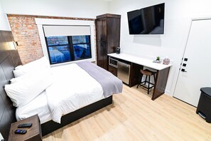 Un dormitorio con cama, escritorio, televisor y ventana con vistas.