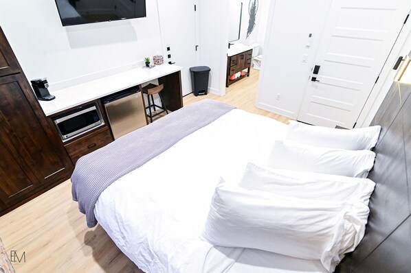 A hotel room with a bed, a desk with a chair, a microwave, a trash bin, and a wardrobe.