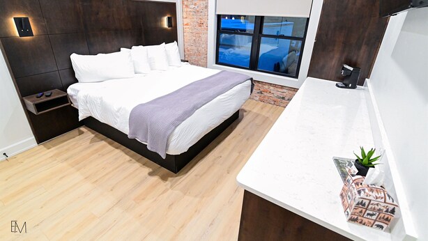 A modern bedroom with a large bed, a nightstand, a small table with a plant, and a window with a view.