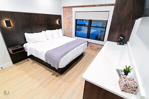 A modern bedroom with a large bed, a nightstand, a small table with a plant, and a window with a view.