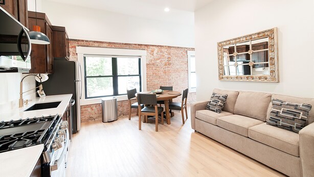 A modern kitchen with a gas stove, wooden cabinets, and a dining area with a brick wall.