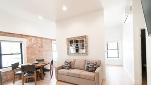 A living room with a beige sofa, wooden chairs, a coffee table, and a brick wall.