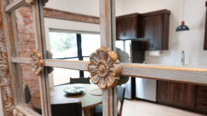 A mirror with ornate floral decorations, a wooden table, and a kitchen area with cabinets and a hanging light fixture.