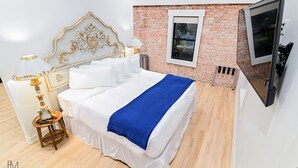 A hotel room with a bed, a TV, a window, and a brick wall.