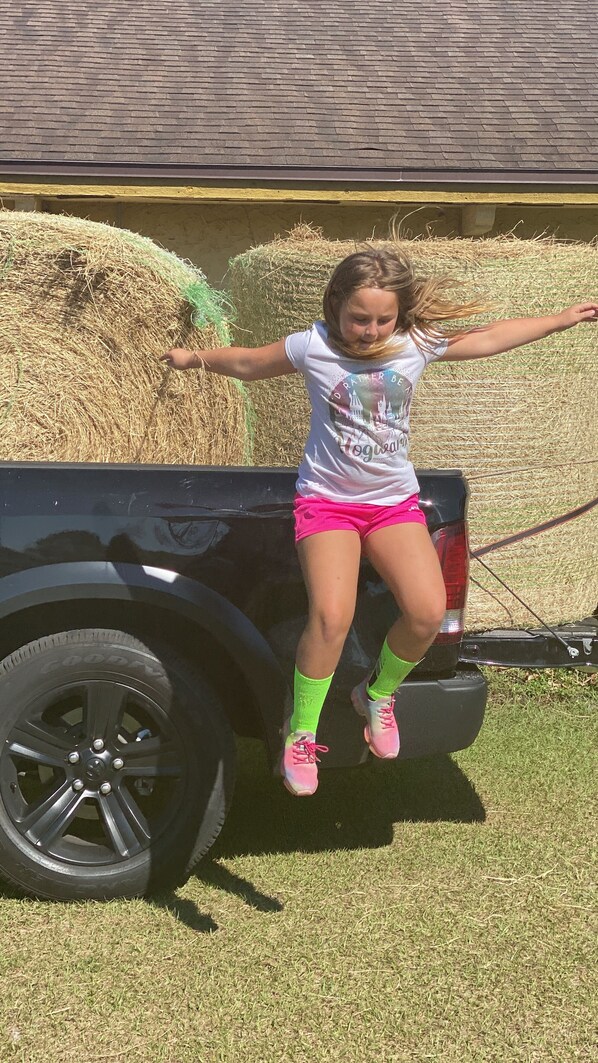 A person sitting on the back of a vehicle with hay bales in the background.