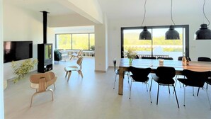 Un vaste espace de vie comprenant une grande fenêtre, une cheminée, une table à manger avec des chaises et un téléviseur.