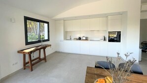 Une cuisine moderne avec des meubles blancs, un four encastré et un coin repas comprenant une table et des chaises en bois.