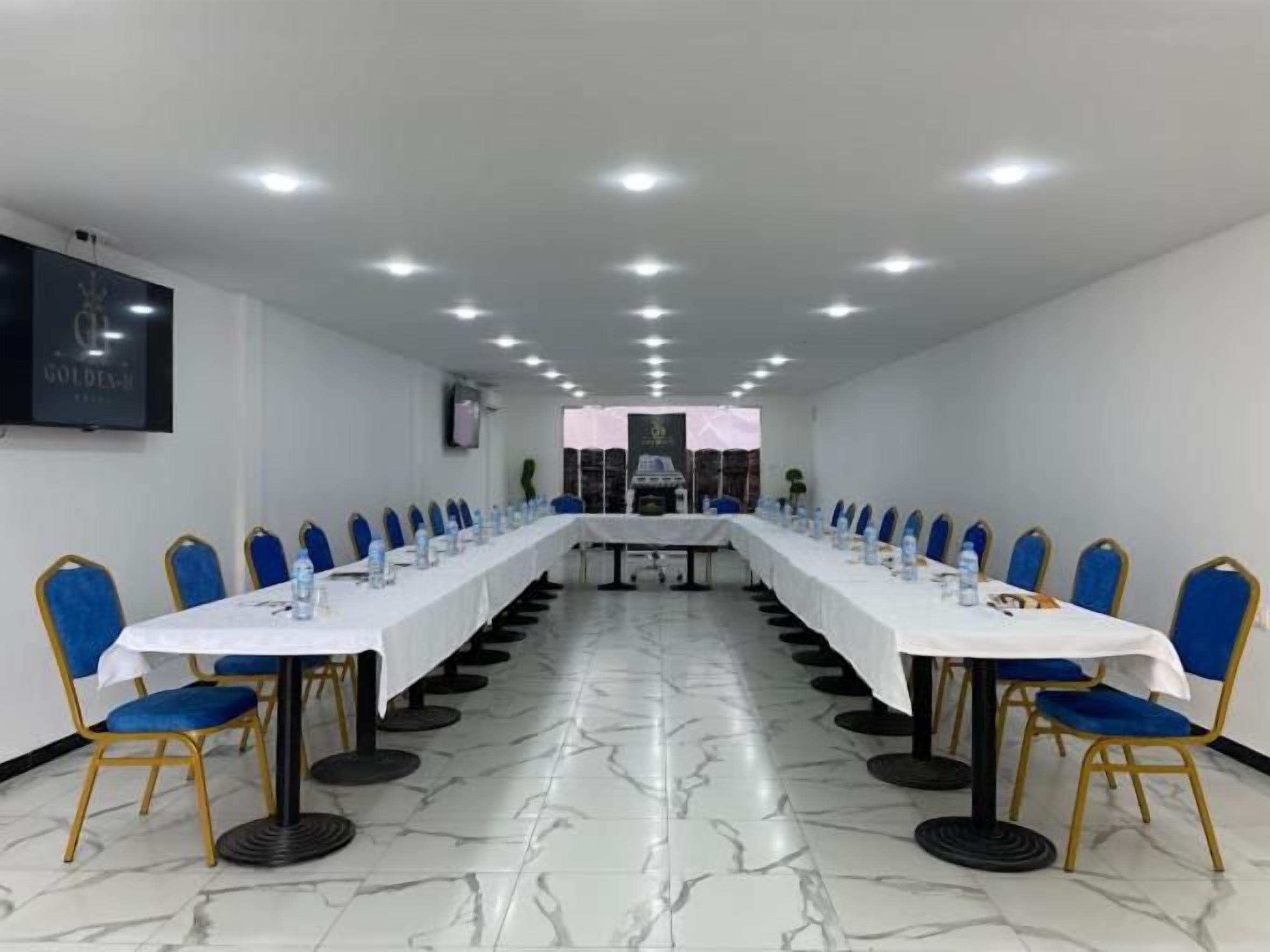 A conference room with a long table, blue chairs, and a white tablecloth.