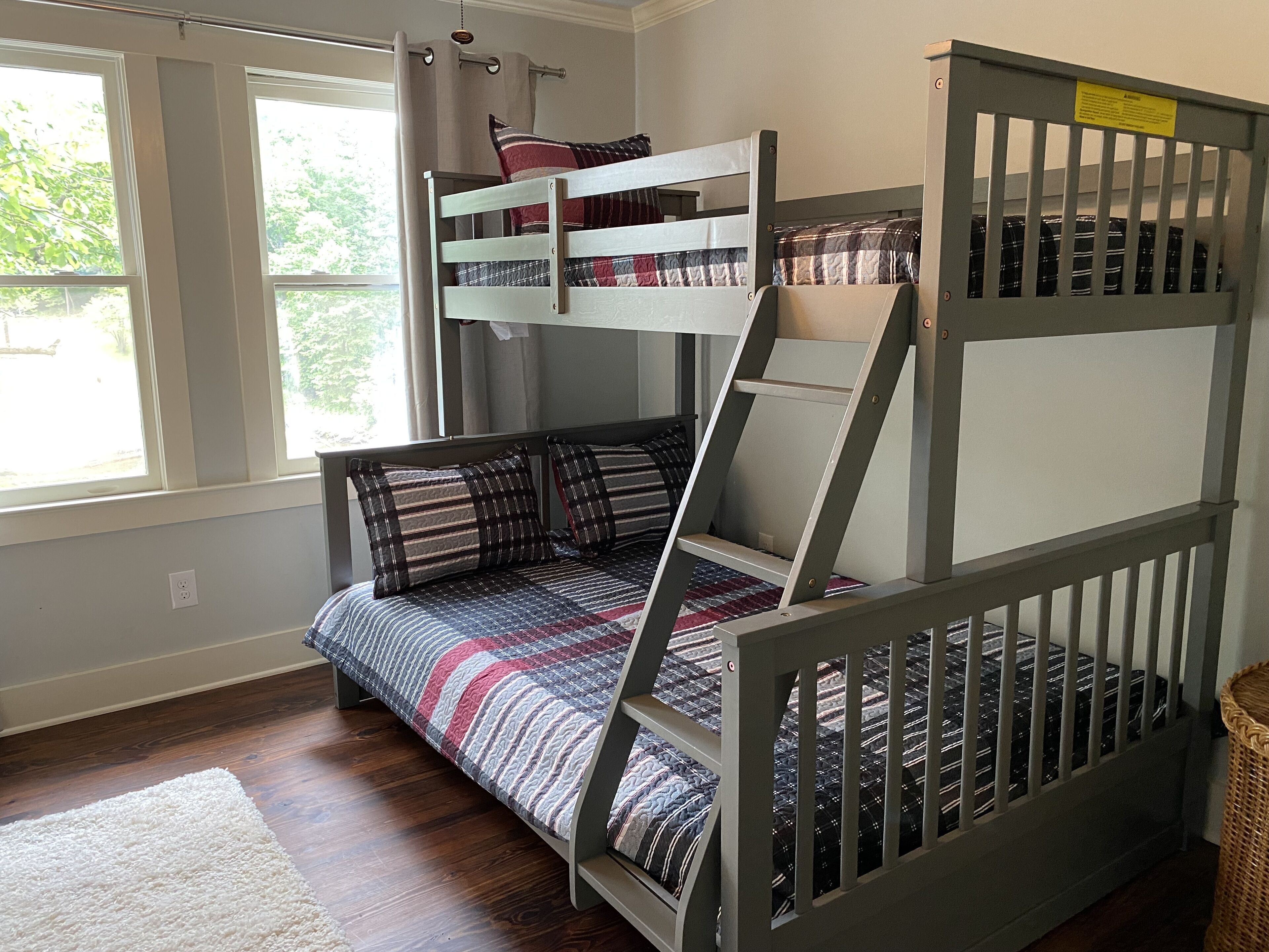A bunk bed with a ladder, a window with curtains, and a rug on the floor.