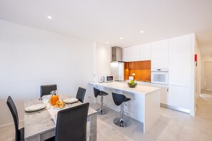 Une cuisine moderne avec des meubles blancs, un îlot central et un coin repas comprenant une table et des chaises.