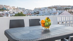 Una mesa con un frutero y dos sillas, con vista a un pueblo costero de edificios blancos.