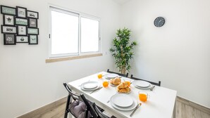 Un comedor con una mesa blanca dispuesta para el desayuno, un reloj en la pared y una planta en la esquina.