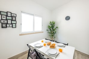 A dining area with a white table set for breakfast, a clock on the wall, and a plant in the corner.