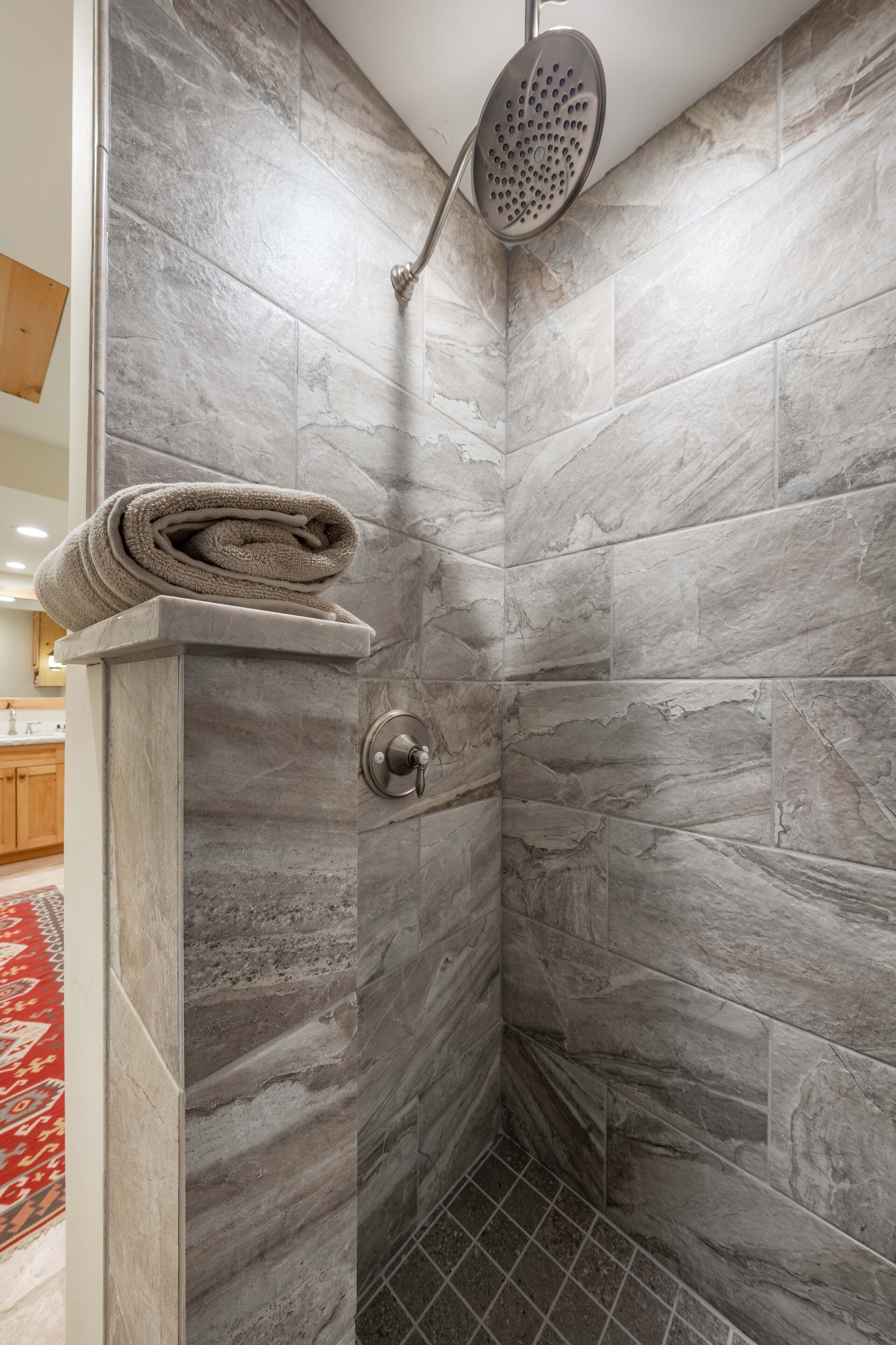 A shower with a handheld showerhead and a towel on a shelf.